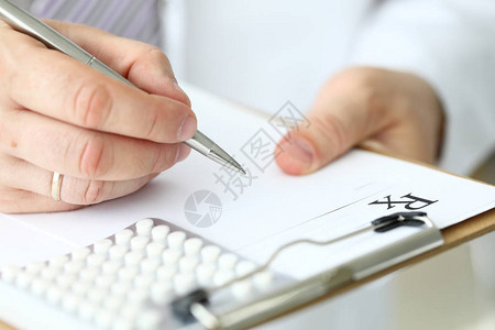 男医生用手臂填写有银笔缝合装置的病人处方表格图片