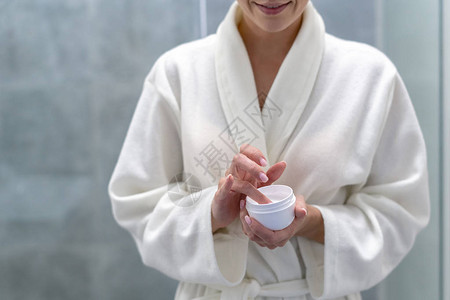 浴袍中年青成年妇女用奶油握在手的罐子上图片