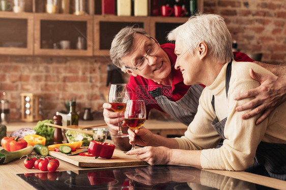 快乐的老年男人和女人在厨房喝着葡萄图片