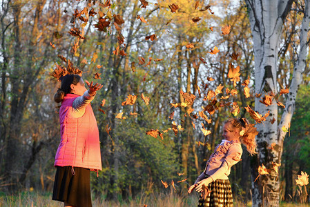 快乐的母亲和女儿扔秋叶在公园图片