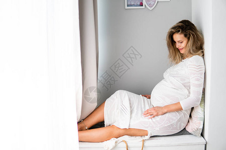 年轻的孕妇坐在床上看着她的肚子期待图片