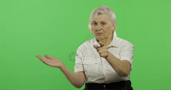 一位老妇人指着镜头微笑一件白衬衫的老俏丽的祖母放置您的徽标或文本色度图片