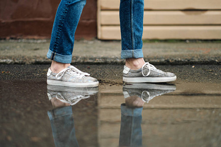 穿着运动鞋的近脚穿行在人行道上的水坑中雨背景图片