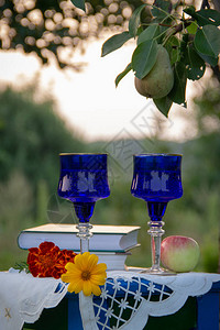 两个玻璃蓝色玻璃杯两本书一个苹果和鲜花站在用桌布装饰的凳子上图片