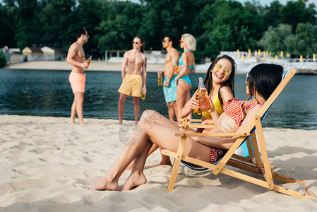 喜悦的多文化女孩在沙滩上朋友附近休息的樱桃图片