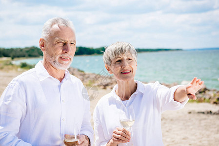 带着葡萄酒杯望海滩的老夫妇笑图片