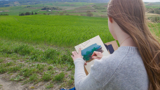 一个才女坐在绿地上画一幅画中景图片