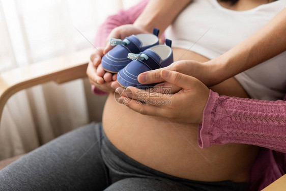 怀孕的夫妻在家里抱着婴儿鞋感受爱和放松产妇和怀图片