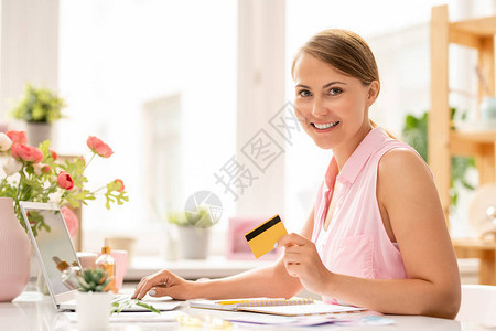 带着塑料卡看着你的快乐年轻有魅力的女士在办公室里做在线图片