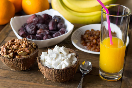 木桌上的美味素食早餐一杯鲜榨橙汁椰子肉和核桃仁从壳碗中取出葡萄干和枣子放在盘子里背景中图片