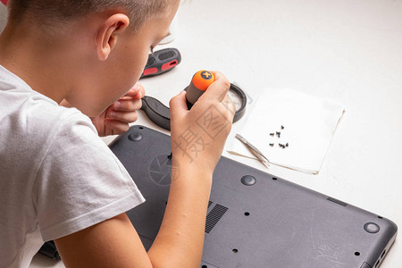 一个10岁的男孩正在整理一台笔记本电脑进行清洁和维护选择焦点框架中的螺丝刀清洗气缸放大镜背景图片