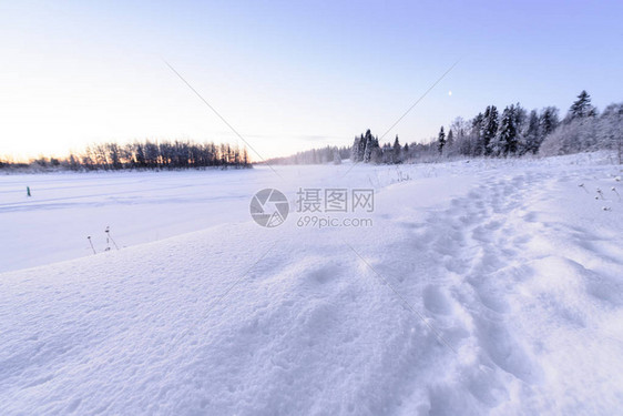 芬兰假日村Kuukiuru的冰湖和森林在冬季被大雪和美丽的蓝天图片