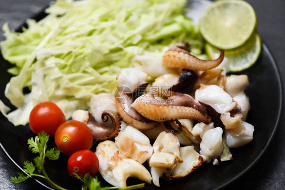 餐桌上配有柠檬香草和香料的鱿鱼沙拉触手章鱼烹制的开胃菜热辣海鲜在餐厅图片