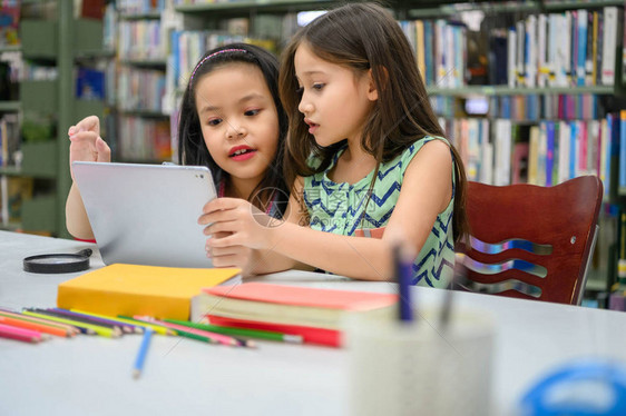 两个快乐可爱的小女孩在学校图书馆的平板电脑计算设备上玩耍教育和自学无线技术概念人们的生活方式和友谊图片
