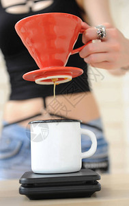 女孩咖啡厅在红色V60的灌注中煮咖啡从手边的漏斗滴水到电子规模的白背景图片