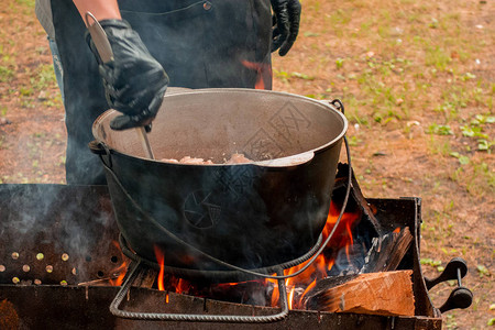 派对野餐时的露天厨房抓饭在户外用火做饭厨师正在用勺子在大锅里搅拌餐盘Bushpot留在金属丝架上和蒸汽上关闭图片