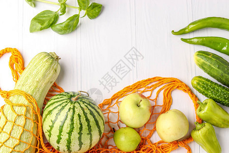 白色背景橙色可重复使用购物网袋中的绿色蔬菜和水果图片