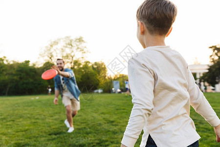 一位快乐的年轻人和他的小兄弟或儿子在公园绿色草场游戏中玩得开心的景象图片