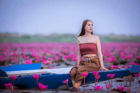 美丽的泰式女孩在红莲花池中快乐地坐在船上背景图片