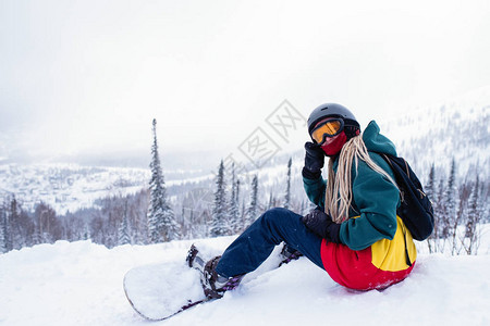 在山上坐着雪坡的滑雪板的女图片