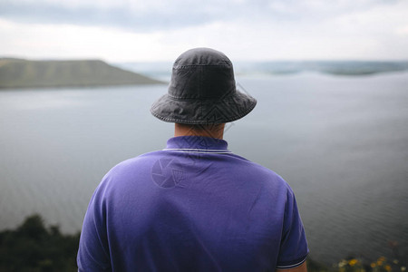 穿着紫色衬衫和渔夫帽的时髦旅行者站在岩石山顶上图片