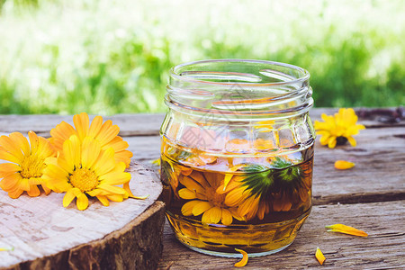 金盏花的酊剂提取物与鲜花在玻璃罐在自然的木制背景上金盏花酊的提取图片