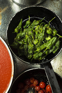 高角观察一些不同煎锅中煮熟的青辣椒和樱桃番茄图片