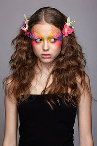 青春少女的肖像和兰花在卷发中年轻女子的化妆和假时尚羽毛图片