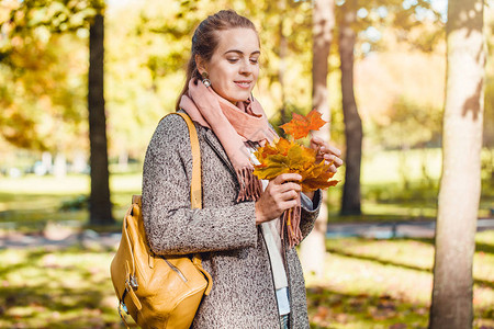 美丽的女人在秋天的公园里拿着黄色的橄榄树叶在户外荡来图片