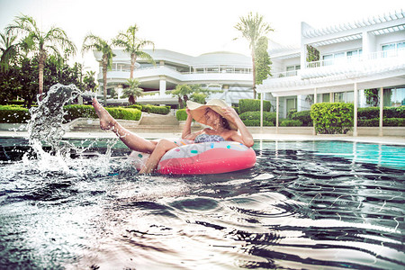 泳池边的暑假一个戴着漂亮大帽子的女人在游泳池里以甜圈的形式在一个充气圆圈上放松溅在他的脚上图片
