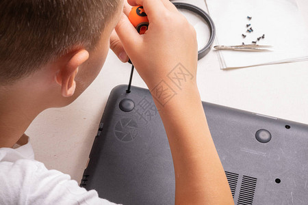 一个10岁的男孩正在整理一台笔记本电脑进行清洁和维护选择焦点框架中的螺丝刀清洗气缸放大镜背景图片