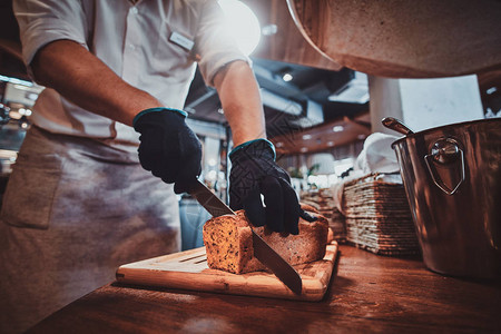 身戴保护手套的富有经验的面包师正在切面包图片