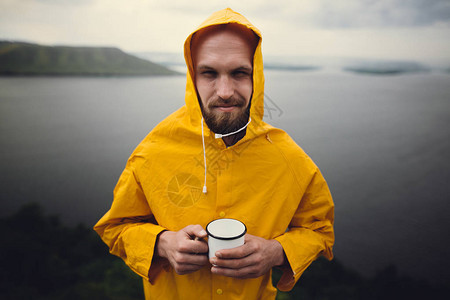 穿着黄色雨衣的时髦旅行者拿着金属杯图片