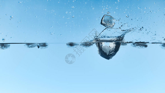 透明的水与落下的冰块和蓝色背景上的飞溅图片