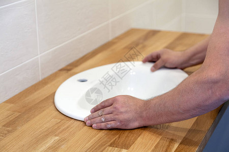 专业水管工在浴室的木桌顶上安装白奥瓦尔陶瓷槽图片