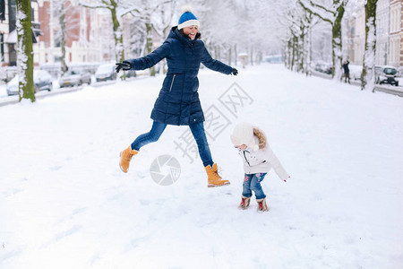 穿着牛仔裤白底外套和编织帽的漂亮女孩与妈一起在户外雪地上跳跃图片