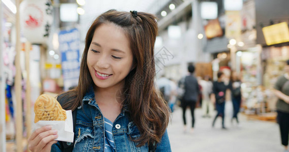 在东京街头吃鲷鱼烧的旅行女人图片