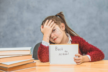 一个灰色背景的小女学生把有文字的纸带回学校女孩低下头图片
