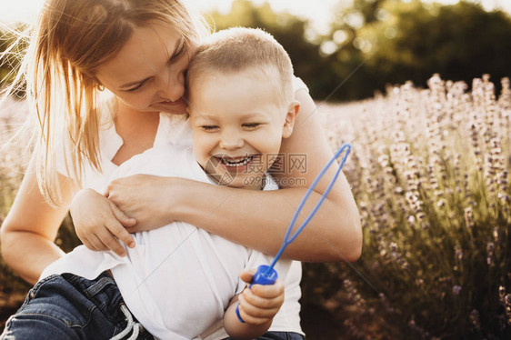 可爱的年轻妈在户外给儿子挠痒美丽的年轻女子在花丛中与她的小男孩图片