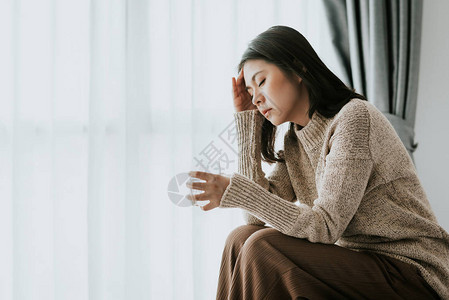 生病的亚裔妇女因感冒和感寒头痛拿杯水图片