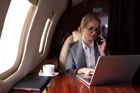 商业女商人在商务旅行中讲智能电话和在飞机上图片