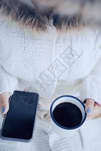 顶视图和特写女人手在寒冷的天气背景下拿着热咖啡和智能手机图片