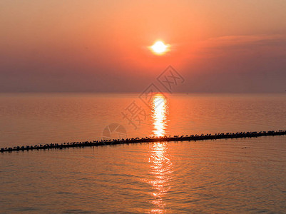 美丽的海上日落海鸥坐在防波堤上夕阳在水面上反射图片