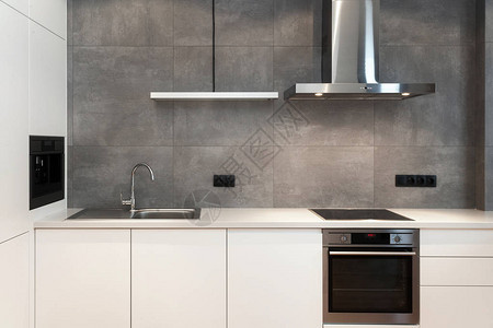 阁楼风格的白色现代厨房的现代室内设计带内置家用电器电炉烤箱台面水槽和灰墙抽油背景图片