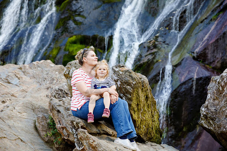 可爱的蹒跚学步的女孩和母亲坐在Powerscourt瀑布的水梯附近图片