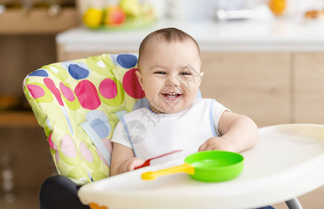 小笑声快乐的婴儿坐在高儿童椅上在图片