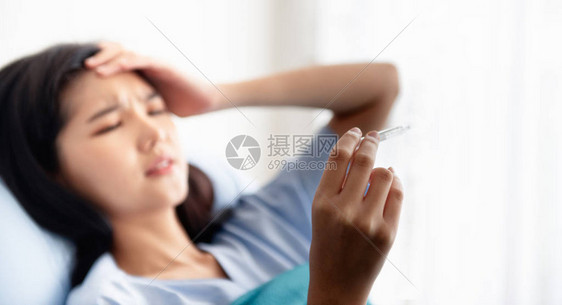 一名躺在医院床顶的年轻女子正在抓取温度计并观察温度计图片