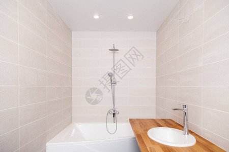 空荡的新浴室配有米色陶瓷矩形瓷砖大浴缸银色淋浴水龙头带陶瓷水槽的木制台面概念维修公寓浴图片