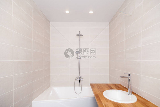 空荡的新浴室配有米色陶瓷矩形瓷砖大浴缸银色淋浴水龙头带陶瓷水槽的木制台面概念维修公寓浴图片