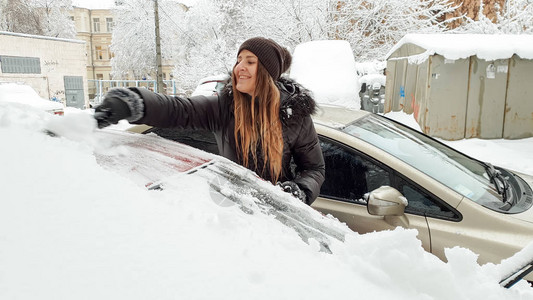 穿着夹克的微笑女孩清理了雪盖车背景图片